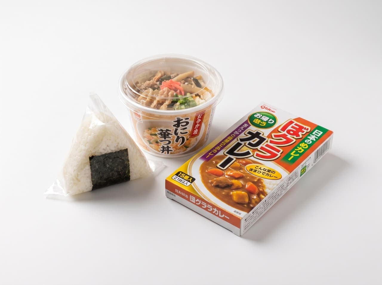Japanese convenience meals: a wrapped onigiri, a rice bowl cup, and a boxed instant curry on a white studio background