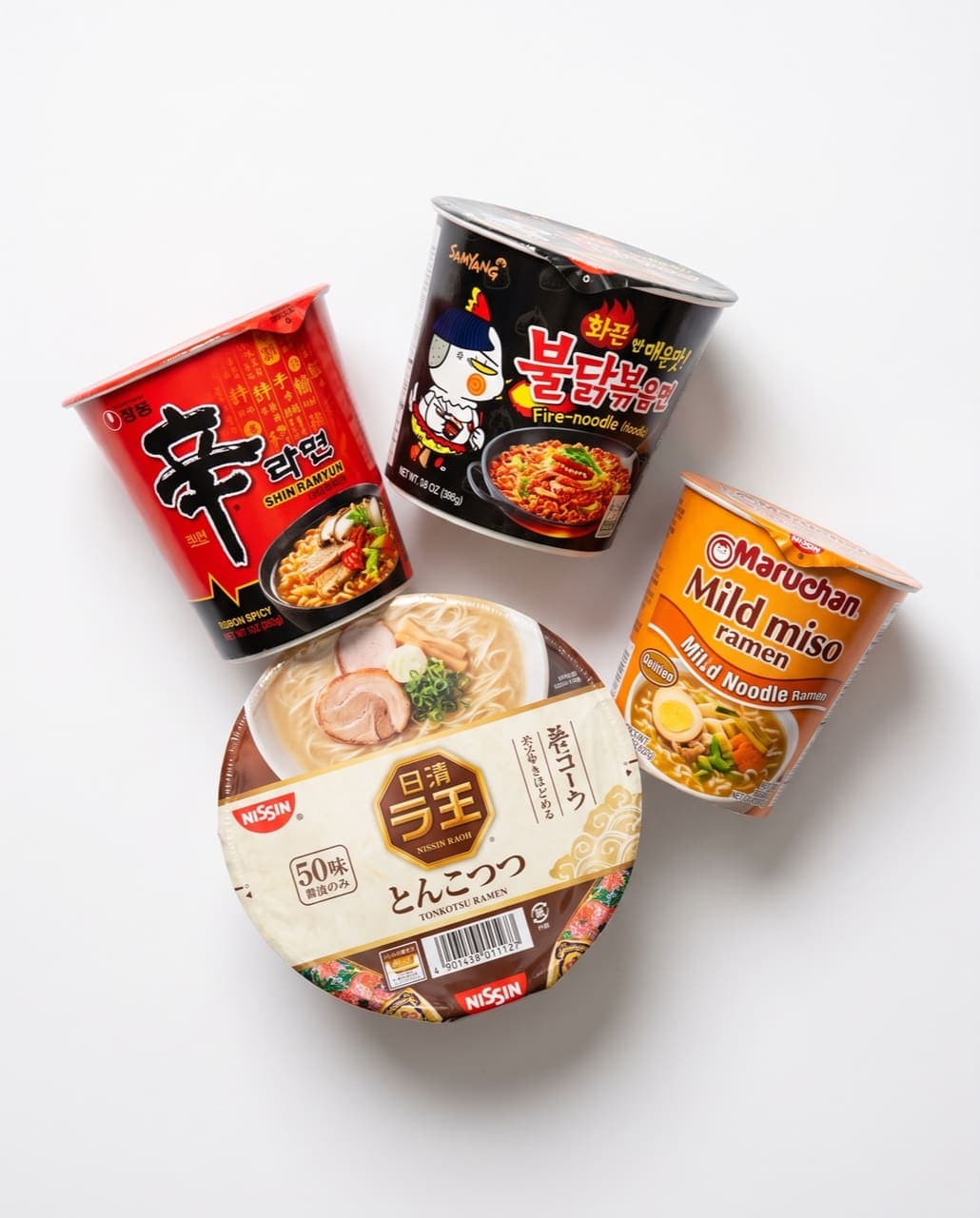 Instant noodle cups: spicy Korean ramyun, fire noodles, tonkotsu ramen bowl, and mild miso ramen on a white studio background